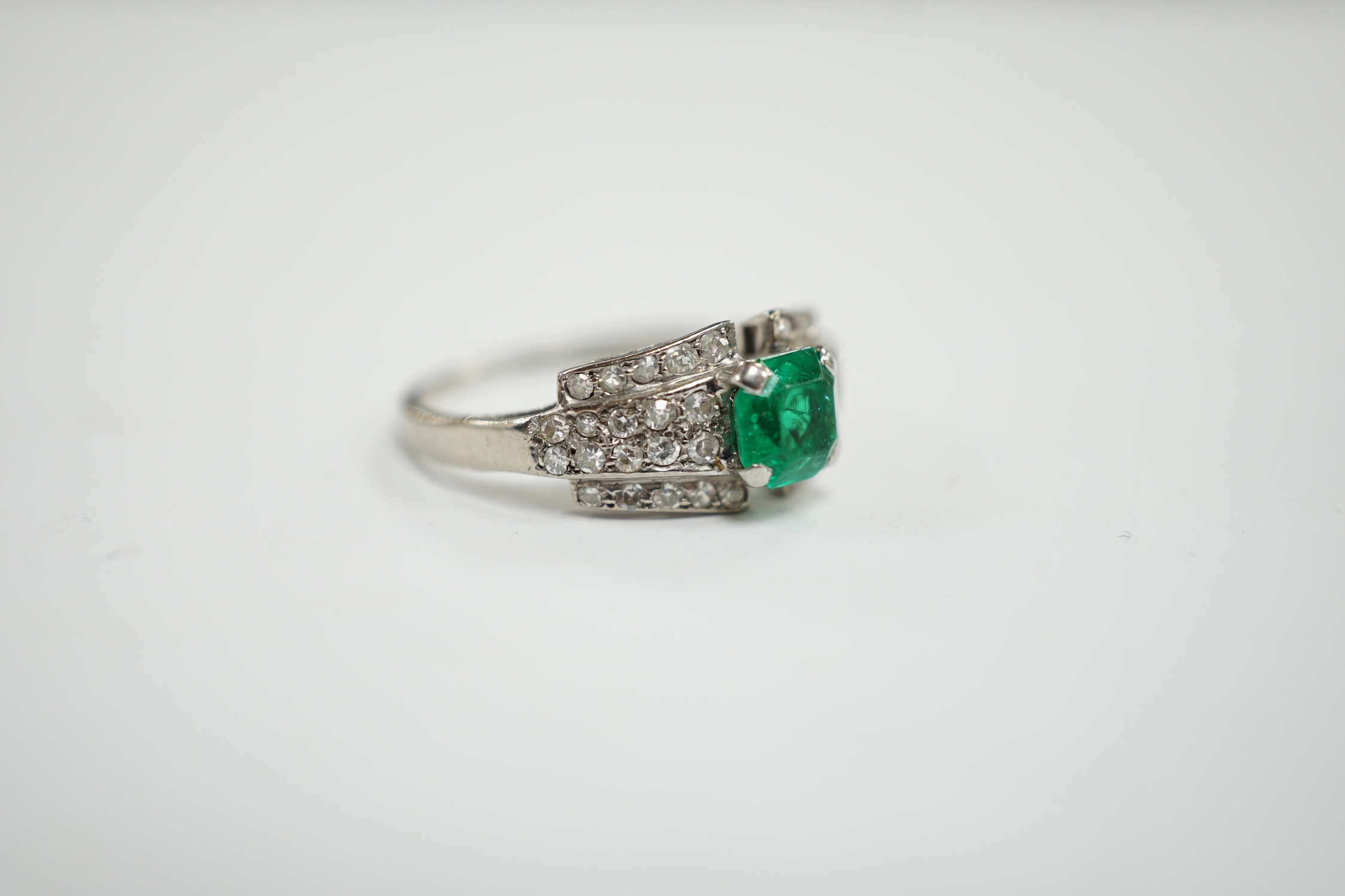 A white metal and octagonal cut emerald set dress ring, with diamond cluster set shoulders, size O, gross weight 3.6 grams.